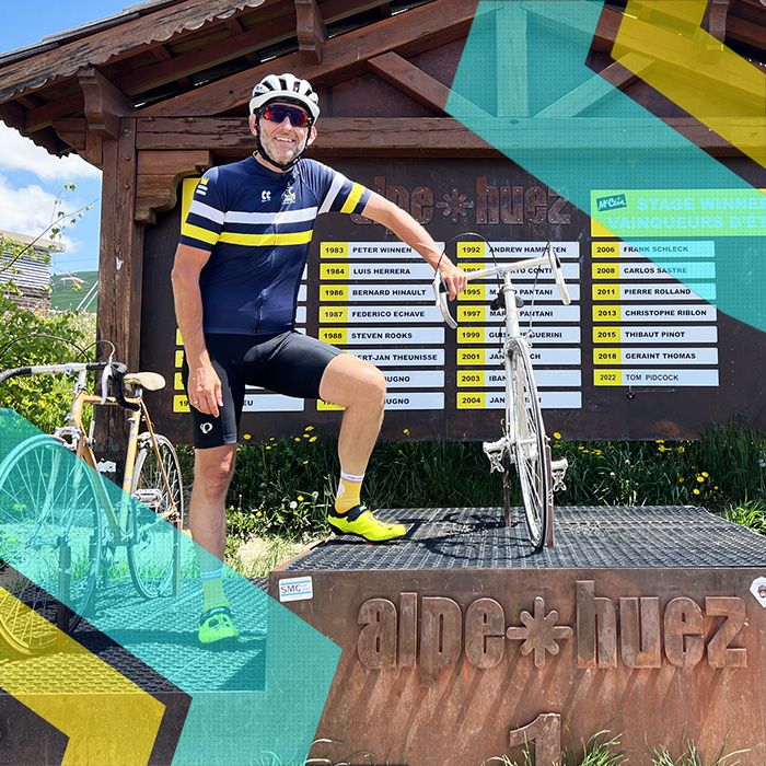 A man is standing in front of a sign for cycling club alpe-huz in Surrey.