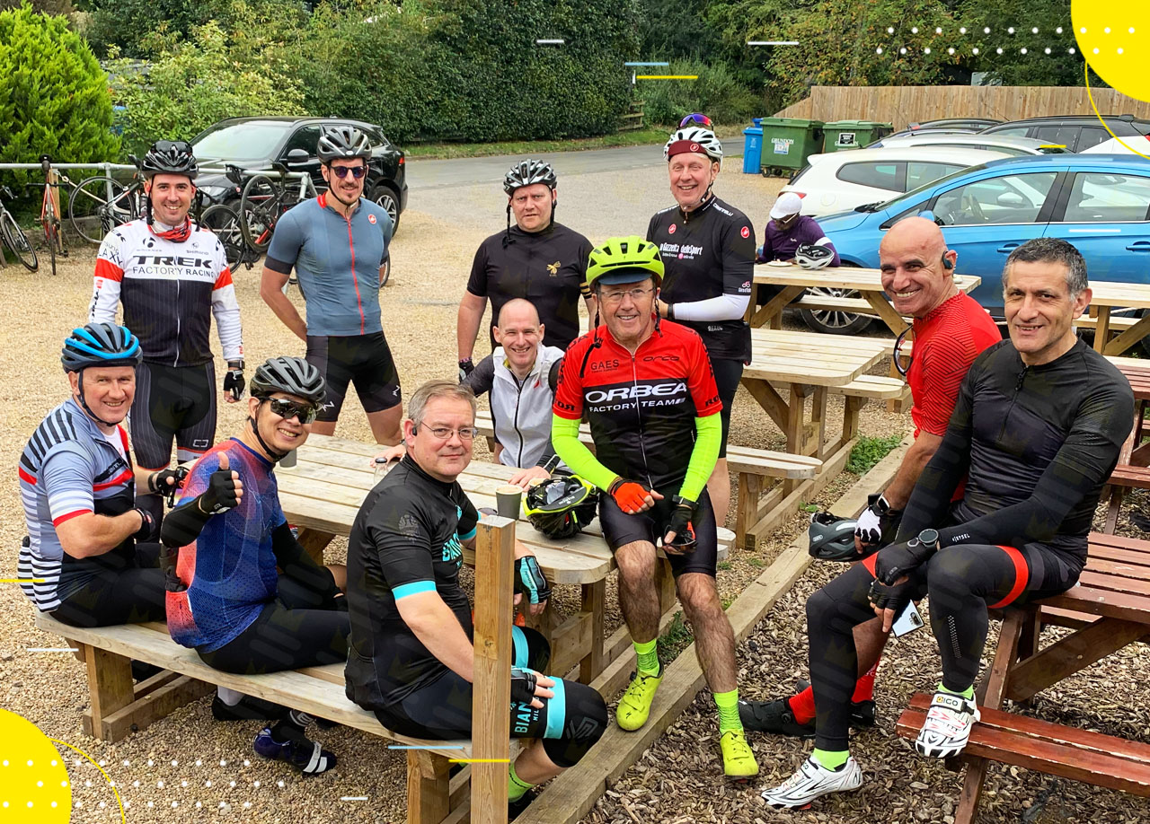 A group of cyclists posing for a photo at a picnic table.